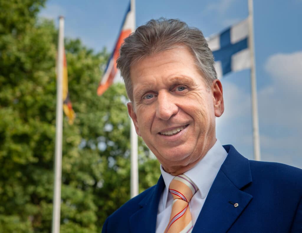 Porträt Bernd Jorkisch vor den Flaggen Deutschlands, Schleswig-Holsteins und Finnlands